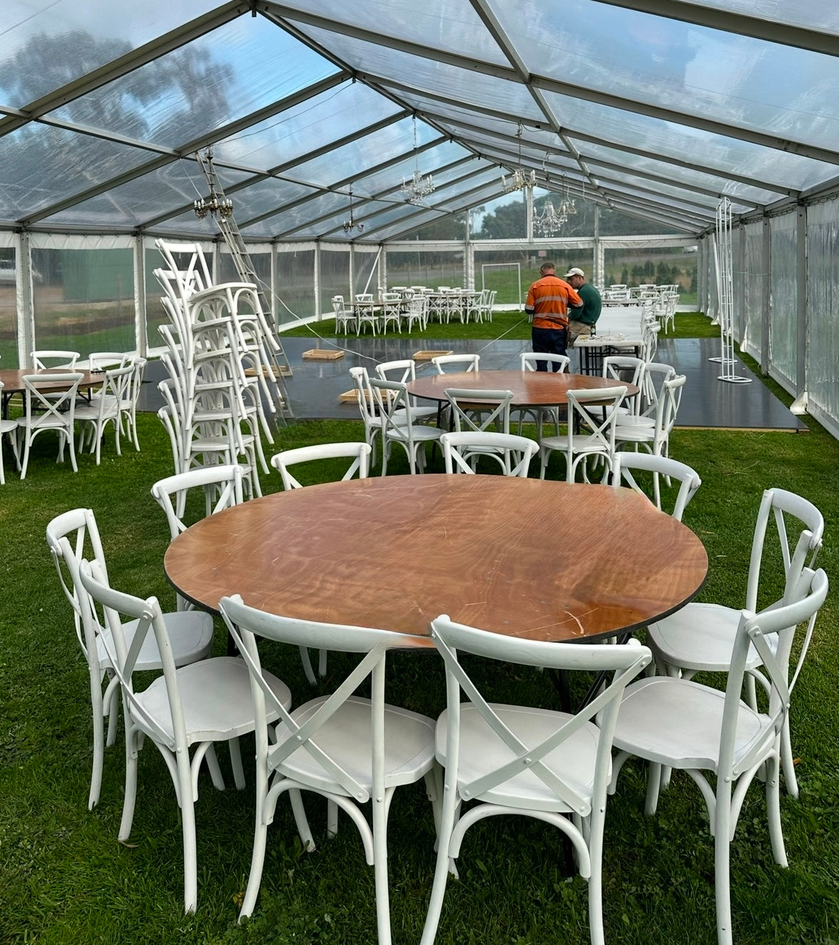 Outdoor event setup with wooden tables and white chairs under a clear tent. South Australia Adelaide Party People. Wedding and Party Hire Equipment. 